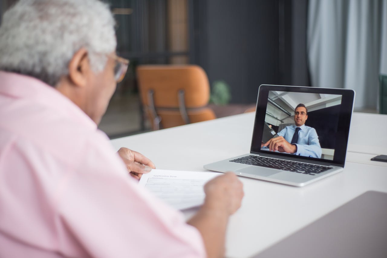 Senior discussing business on a video call with a consultant on a laptop.